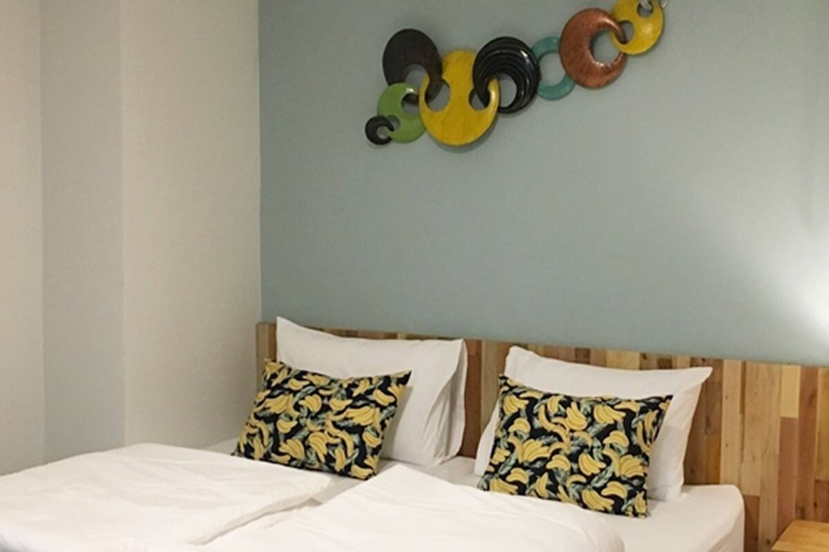 A double bed with white linens, two pillows with a yellow and black pattern, and a wooden headboard.