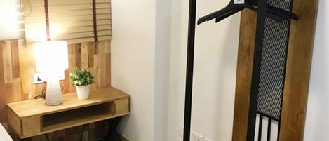 A room with a bed, a bedside table with a lamp, a potted plant, and a wooden coat rack.