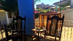 Ein Balkon mit zwei Holzstühlen und einem kleinen Tisch, umgeben von einem Metallgeländer und einer blauen Wand.
