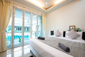 A hotel room with a large bed, a view of a pool, and a balcony. - The Ananas Serviced Apartments (Karon)
