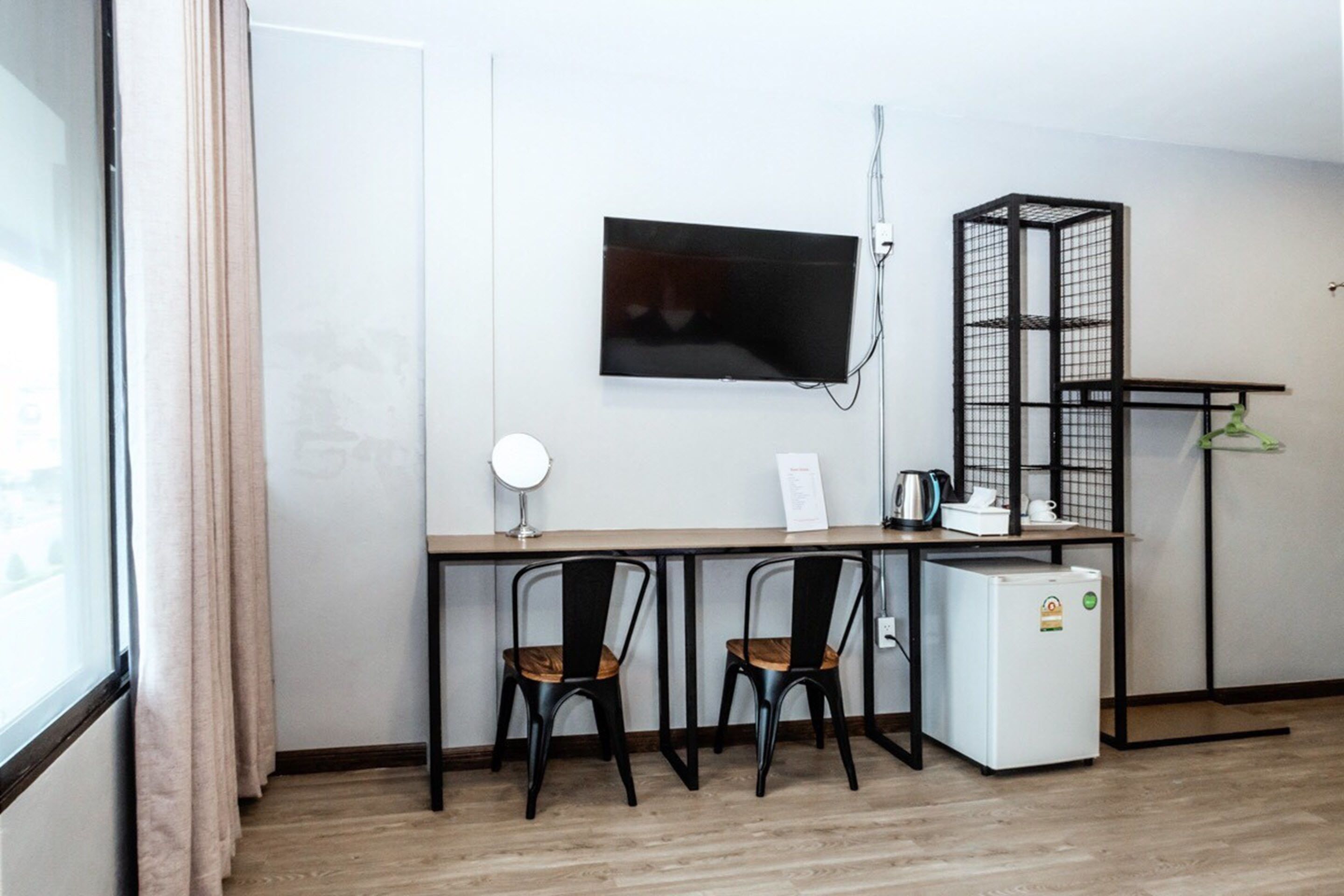 Una pequeña kitchenette con un refrigerador, un microondas y una tetera sobre la encimera. Hay dos sillas y una mesa frente a la encimera. Un televisor está montado en la pared encima de la encimera.