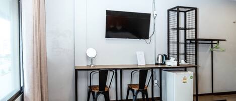 Una pequeña kitchenette con un refrigerador, un microondas y una tetera sobre la encimera. Hay dos sillas y una mesa frente a la encimera. Un televisor está montado en la pared encima de la encimera.