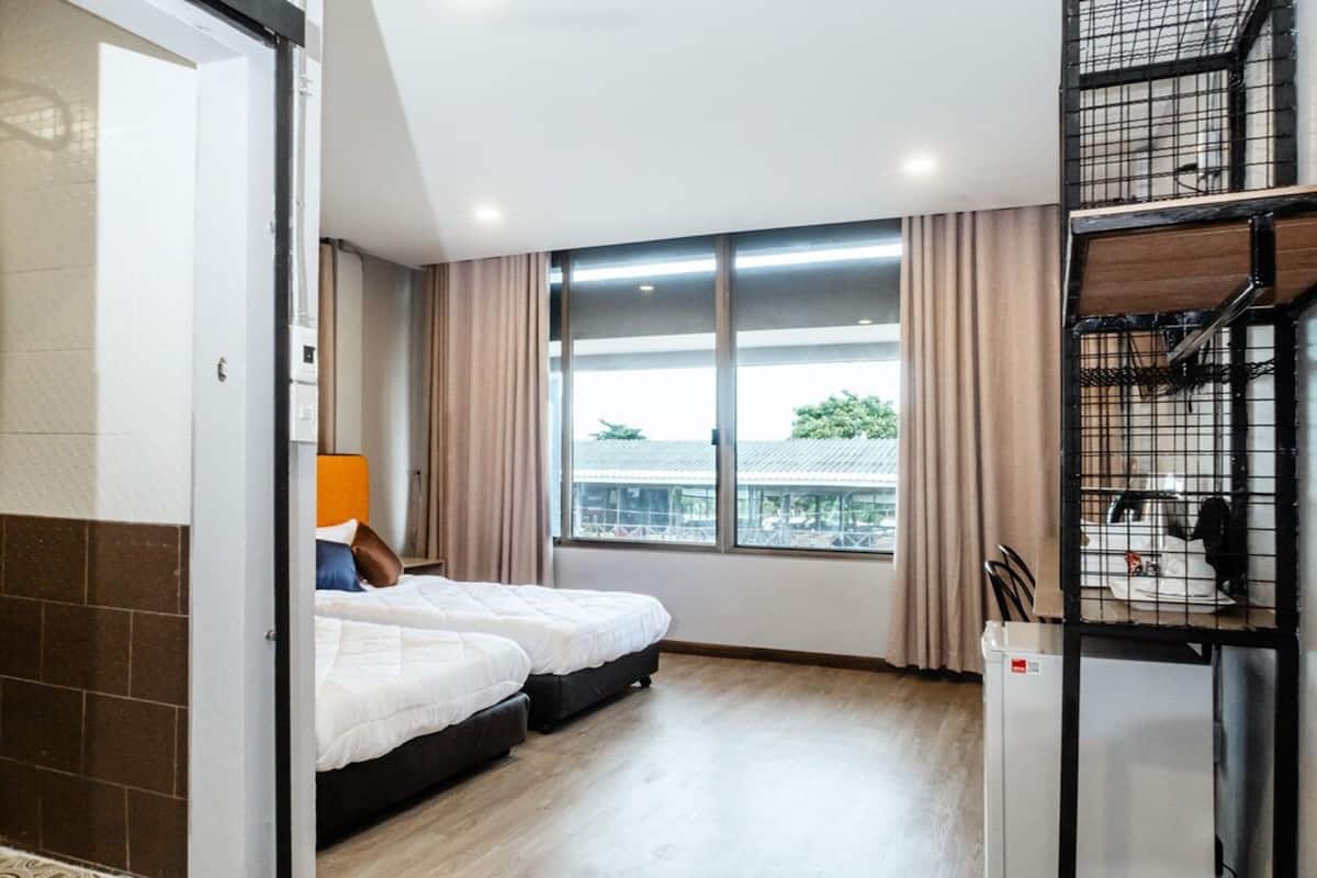 Een hotelkamer met twee bedden, een raam met gordijnen, een kitchenette en uitzicht op buiten.
