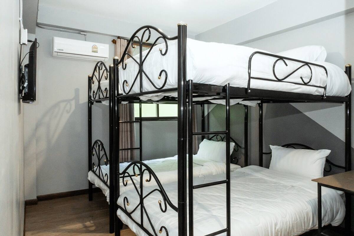 Een slaapkamer met een stapelbed, een houten vloer, een kleine tafel en een wandairconditioner.