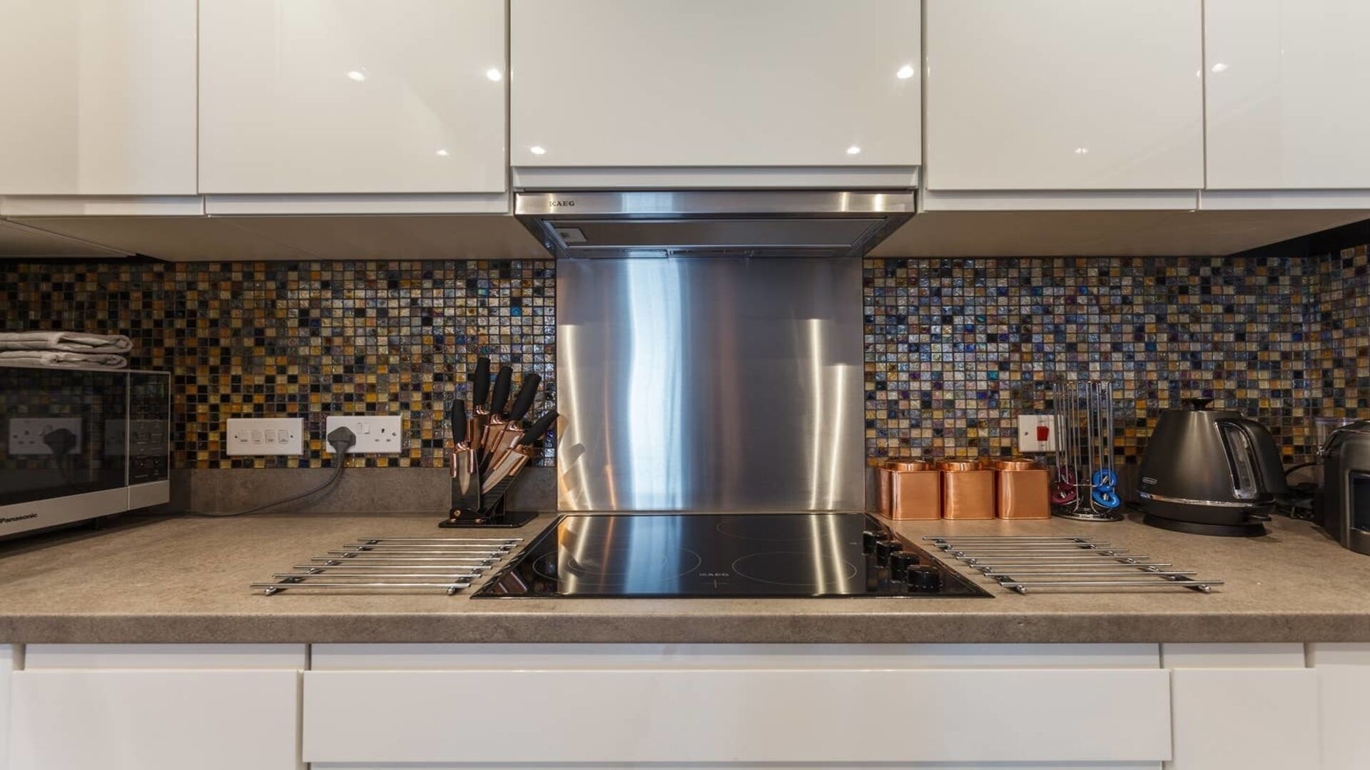 A modern kitchen with a stainless steel range hood, a tiled backsplash, and a built-in oven.