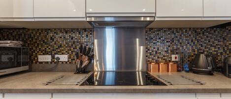 A modern kitchen with a stainless steel range hood, a tiled backsplash, and a built-in oven.