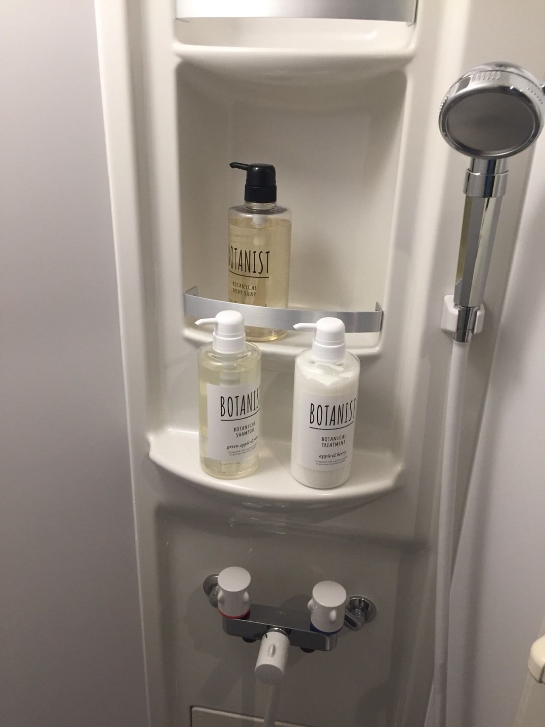 A bathroom with a white sink, a mirror, and three bottles of Botanist body wash and shampoo.