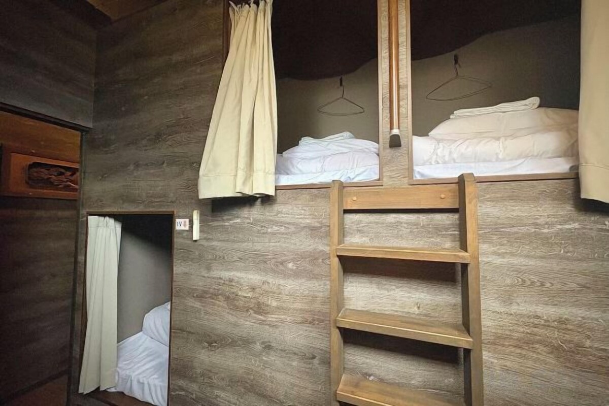 A wooden bunk bed with a ladder, a hanging light fixture, and a mirror.