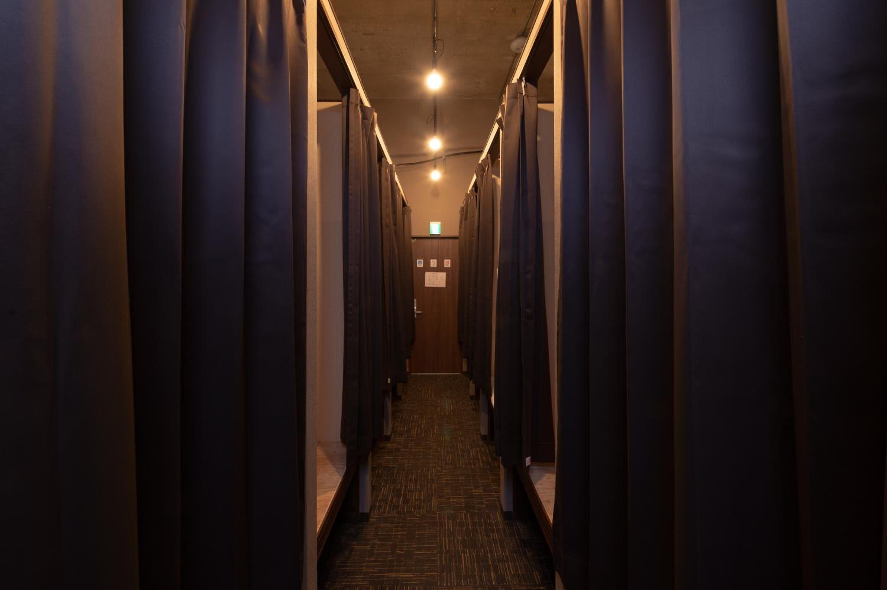 A corridor with multiple stalls, each with a curtain, leading to a door at the end.