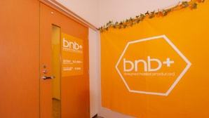 Un corridoio con una parete arancione che presenta il logo 'bnb+' e un'indicazione del prezzo di ¥2.500 a notte.