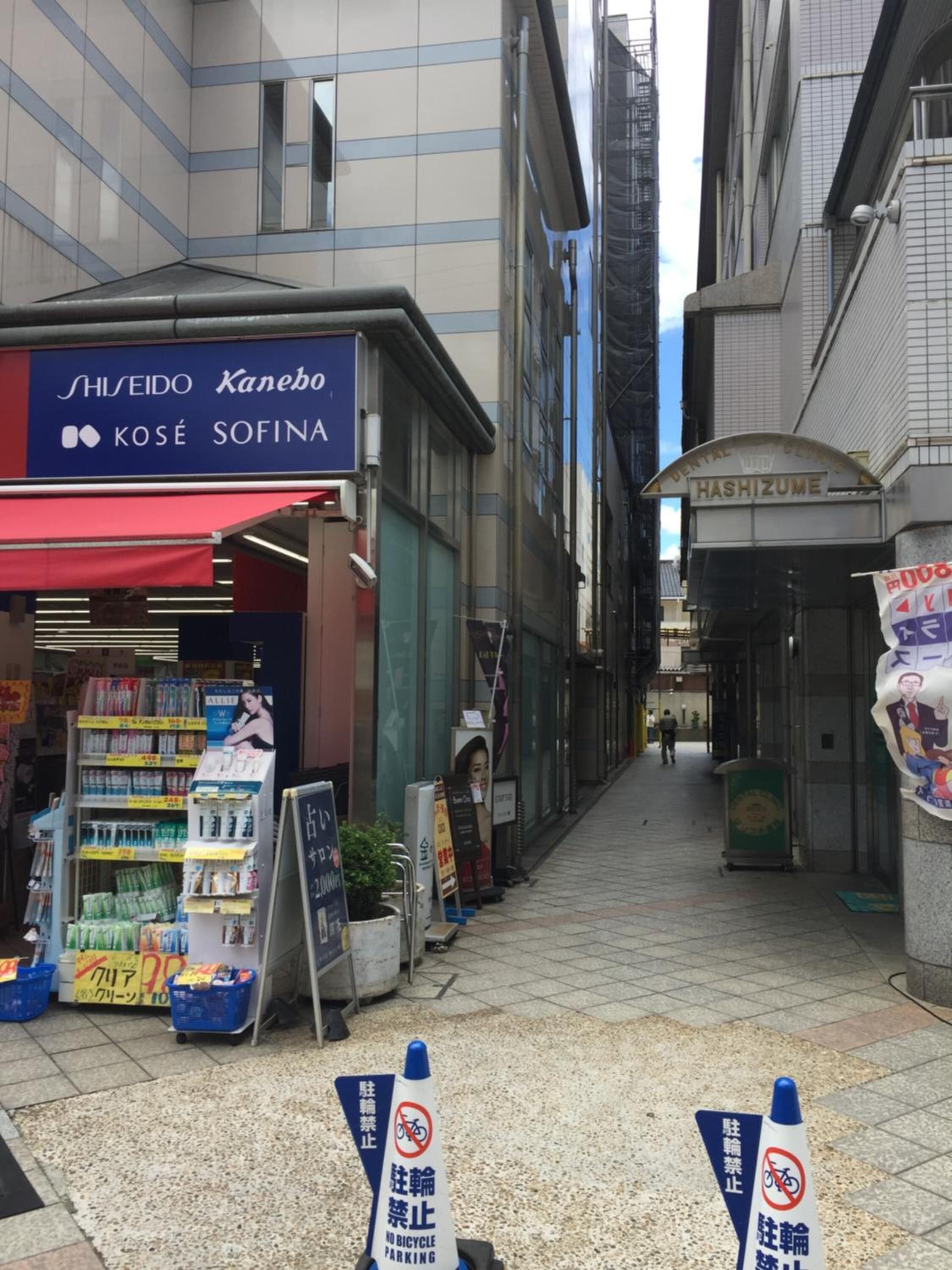 A narrow urban street with storefronts, including a pharmacy and a dental clinic.