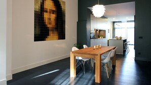 A modern dining area with a wooden table and chairs, a large pixelated artwork on the wall, and a kitchen in the background.