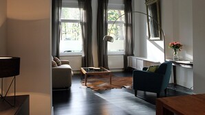 A living room with a sofa, a coffee table, a blue armchair, a lamp, and a vase with flowers.