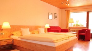 Una habitación de hotel con una cama de madera, dos lámparas de noche, una silla roja y una ventana con cortinas.