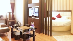 A modern hotel room with a bed, a TV mounted on a wooden panel, a glass coffee table, and a seating area with a chair and a small table. - Zhu Ying Art Hotel (Guangzhou)