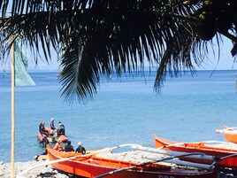 Escena de playa con varias embarcaciones pequeñas y gente en la orilla.