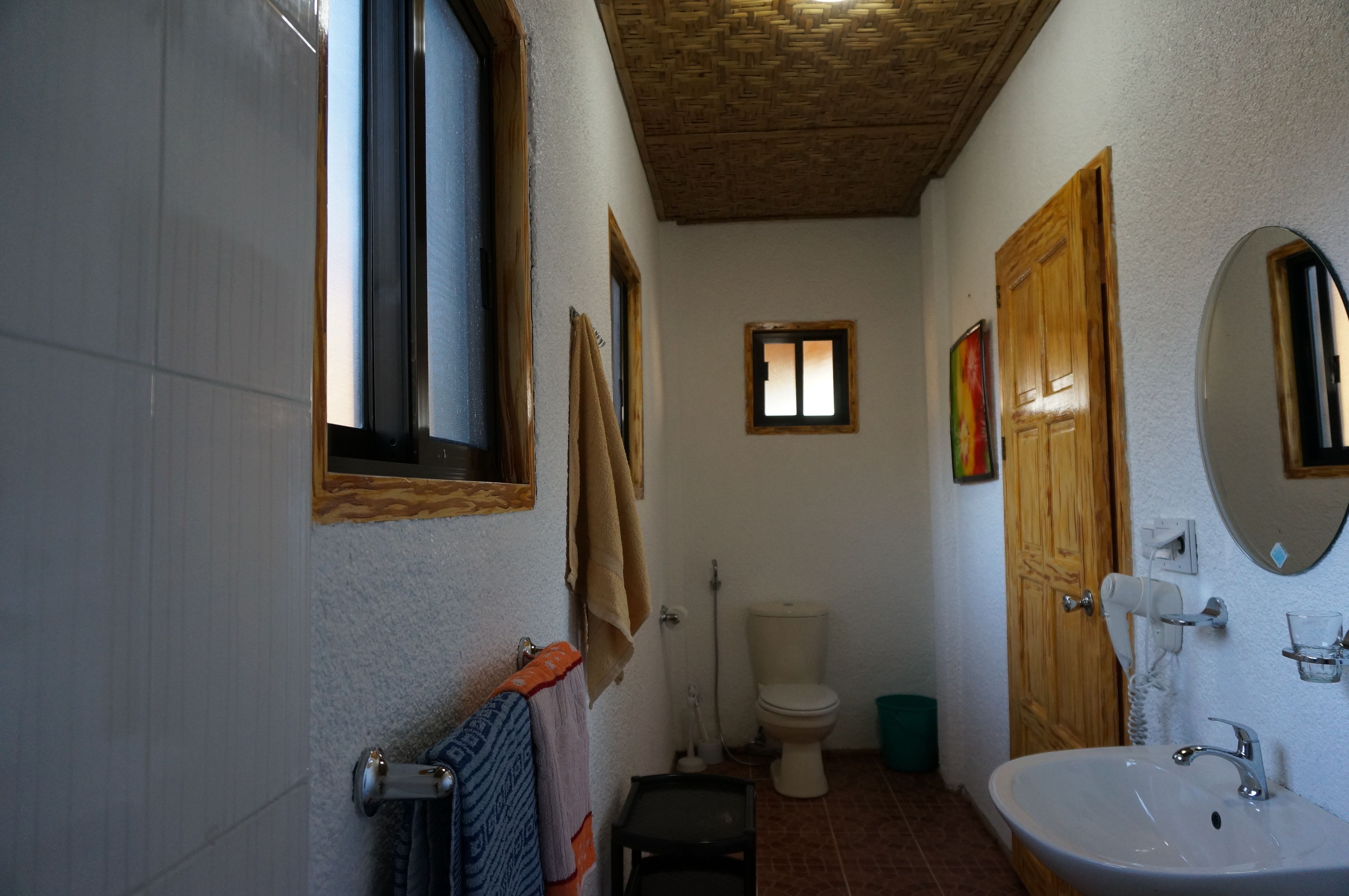 Un baño con lavamanos blanco, puerta de madera y una ventana pequeña.