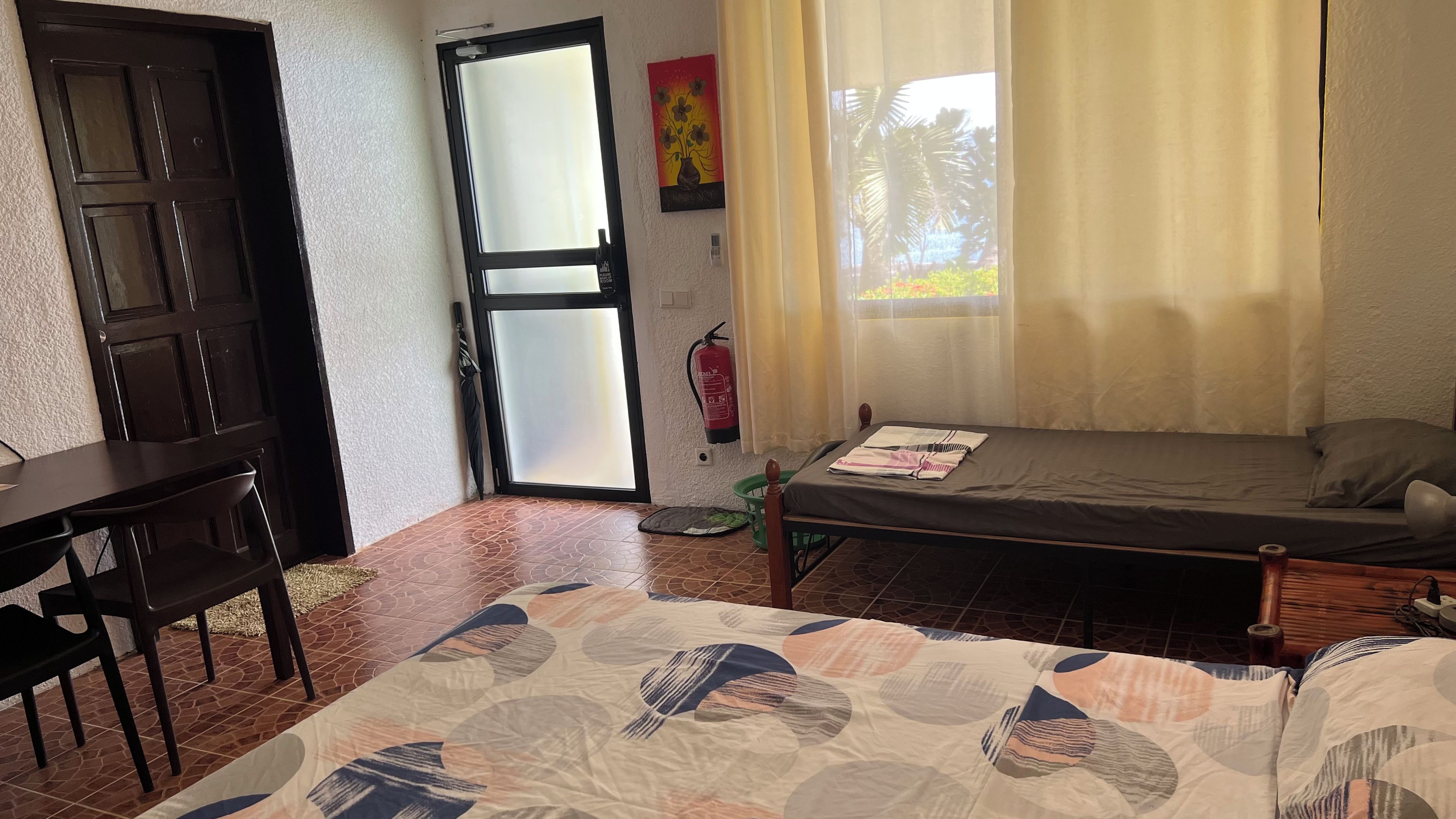 Una habitación con cama, escritorio, silla, extintor y ventana con cortinas.