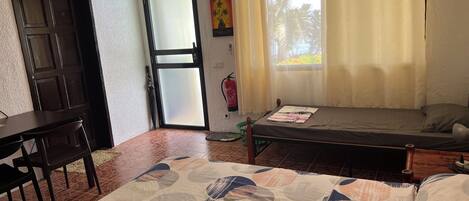 Una habitación con cama, escritorio, silla, extintor y ventana con cortinas.