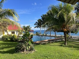 Una piscina con vista al océano, rodeada de palmeras y un edificio de techo rojo.