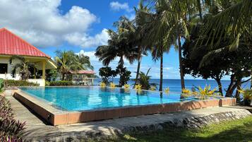 Una piscina infinita con vista despejada al océano, rodeada de palmeras y un edificio con techo rojo.