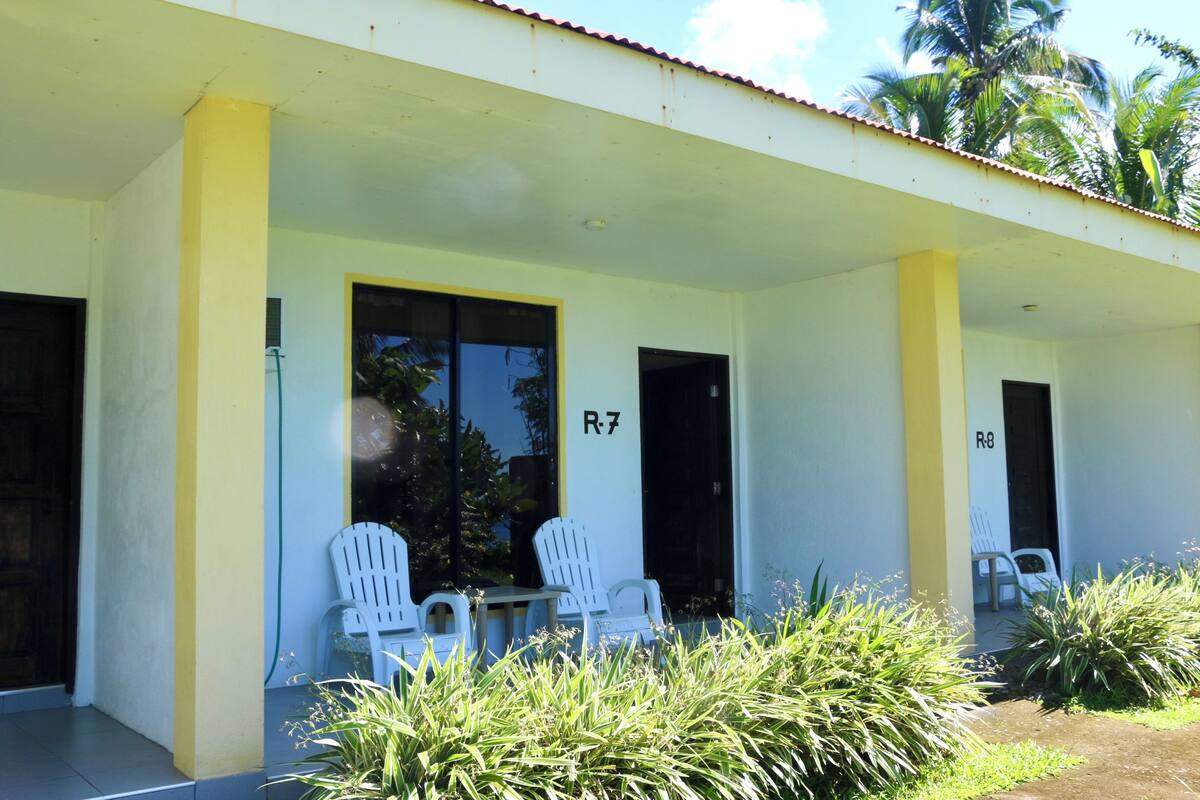 Un edificio con fachada amarilla, dos sillas blancas en el exterior y una puerta con la etiqueta R7.