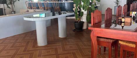 A spacious room with a wooden herringbone floor, a central island with seating, a dining table with chairs, and a bar area with a counter and shelves of bottles.