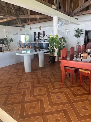 A spacious room with a wooden herringbone floor, a central island with seating, a dining table with chairs, and a bar area with a counter and shelves of bottles.
