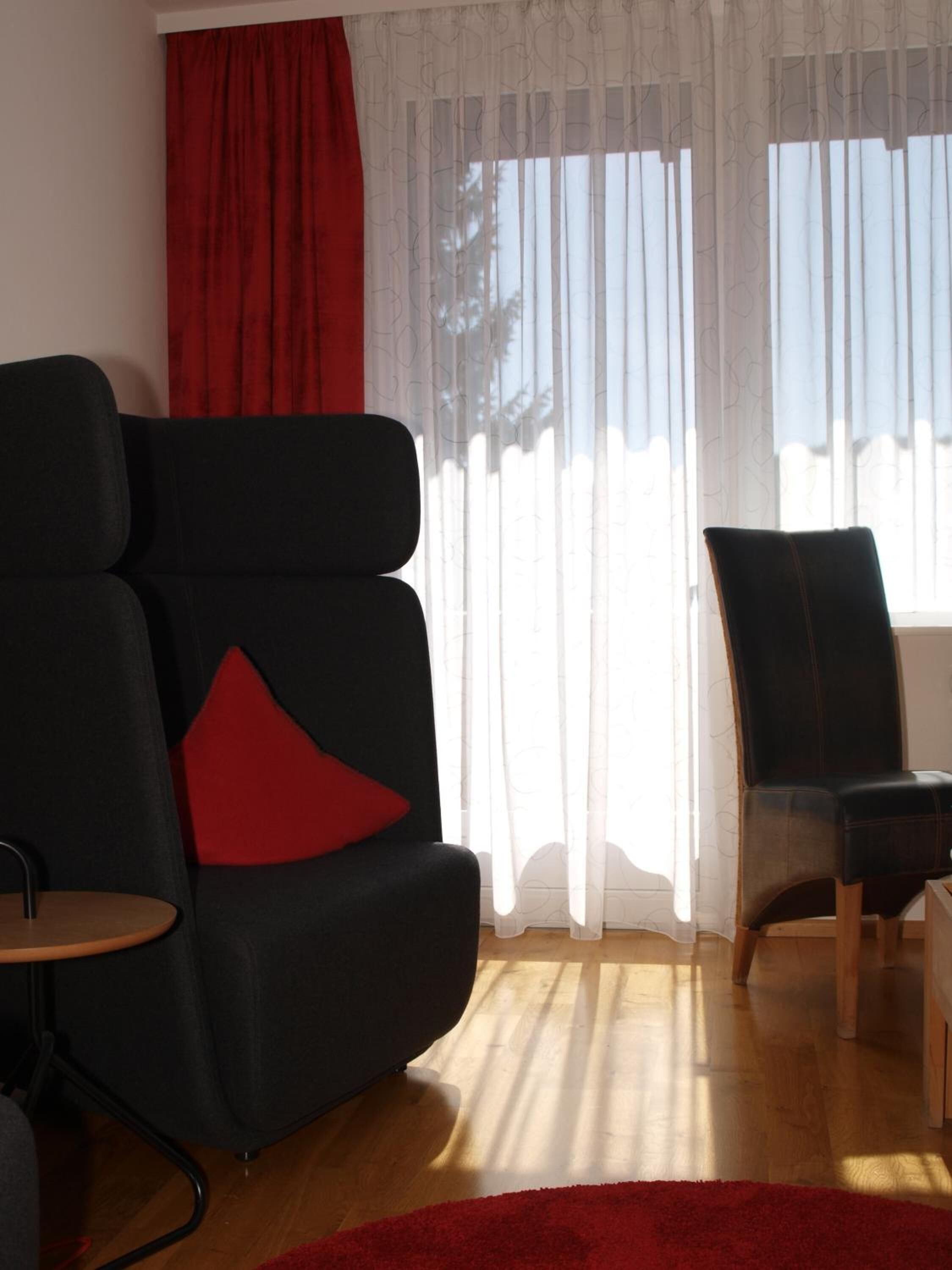 A modern living room with a black sofa, a red pillow, and a wooden coffee table.