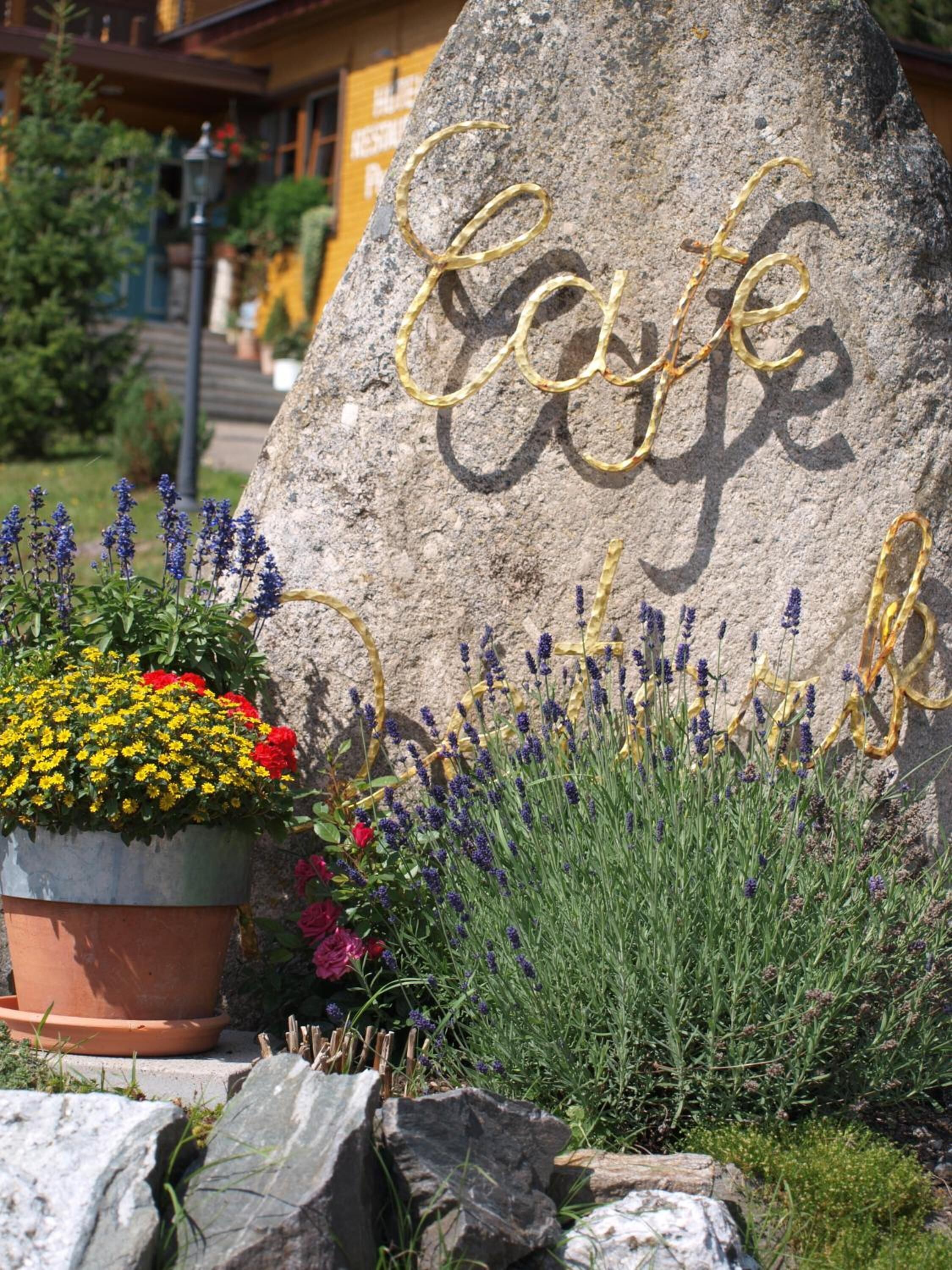 Een grote rots met de tekst 'Cafe' erin gekerfd, omringd door verschillende planten en bloemen.