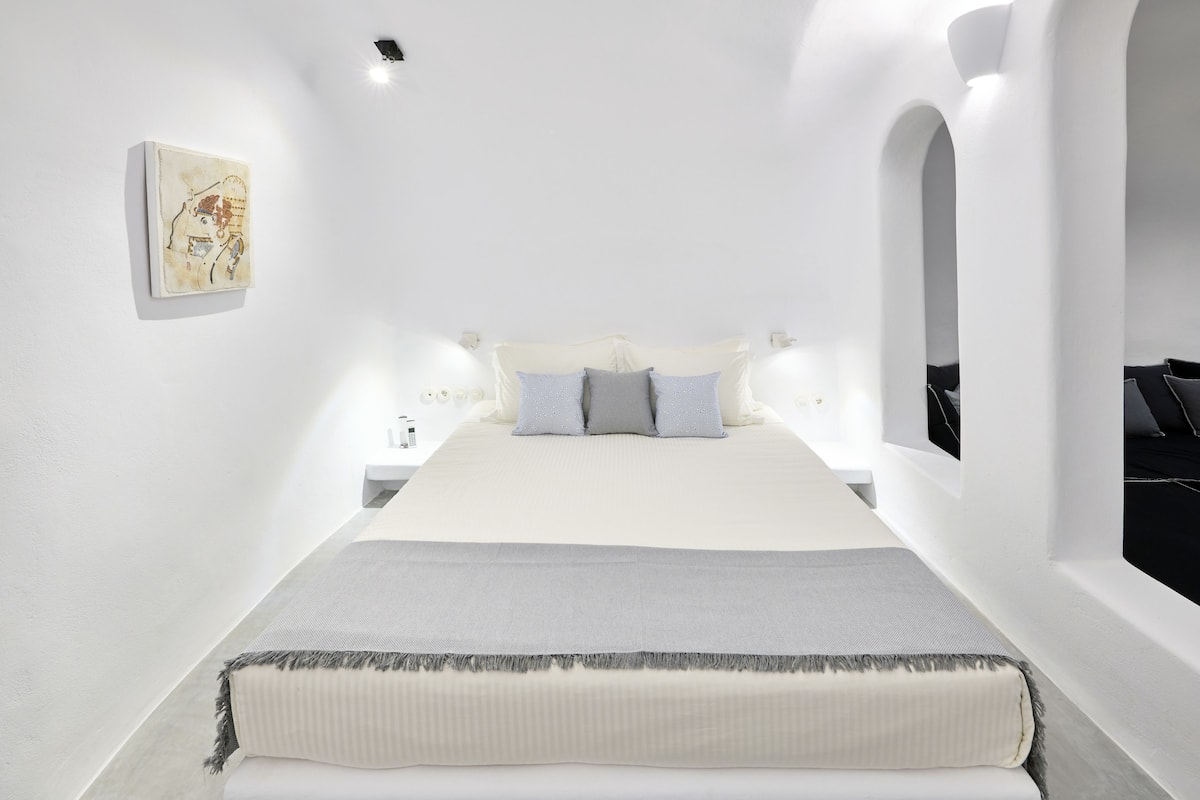 A modern bedroom with a large bed, white walls, and a painting on the wall.