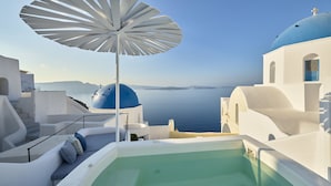 Una piscina infinita blanca con una sombrilla blanca, paredes blancas y cúpulas azules al fondo.