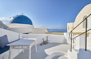 Ein weißer Außenbereich zum Sitzen mit Tisch und Bänken, mit Blick auf einen klaren blauen Himmel und das Meer.