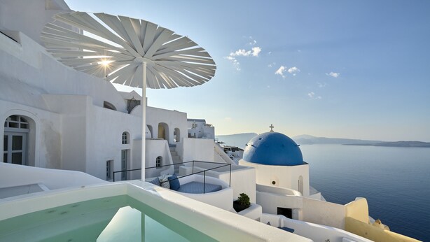 Un edificio blanco con cúpula azul y una sombrilla grande, con vistas a una masa de agua.