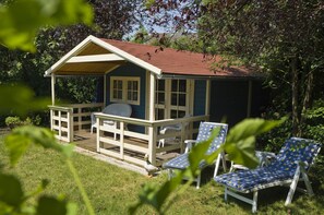 A wooden deck with two lounge chairs and a small building with a red roof. - Hotel Petersen (Bad Zwischenahn)