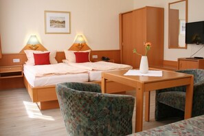 A hotel room with a bed, two bedside lamps, a TV, a wardrobe, and two patterned chairs. - Hotel Petersen (Bad Zwischenahn)