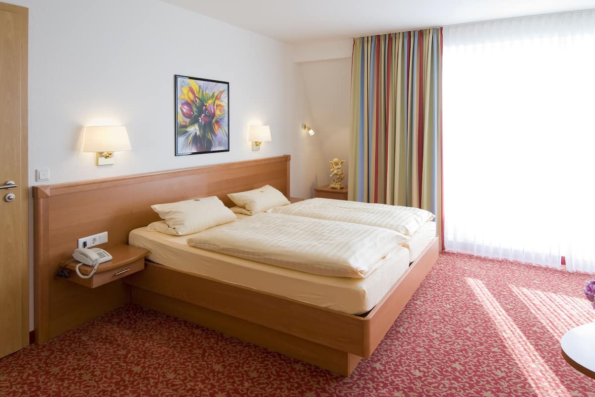 Una habitación de hotel con una cama doble, lámparas de noche, un teléfono, un cuadro y una cortina a rayas.