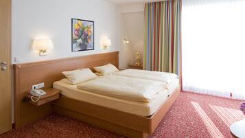 A hotel room with a double bed, bedside lamps, a telephone, a painting, and a striped curtain.