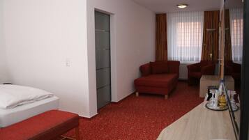 A hotel room with a bed, a red sofa, a desk with a mirror, and a window with curtains.
