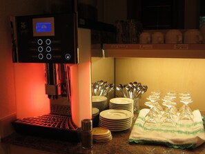 A coffee machine with a digital display, stacked plates, and a cloth napkin on a kitchen counter. - Hotel Petersen (Bad Zwischenahn)