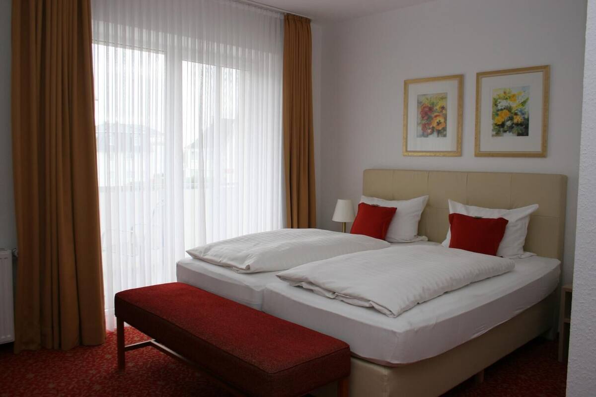 Habitación de hotel con dos camas, un banco y dos cuadros con motivos florales en la pared.