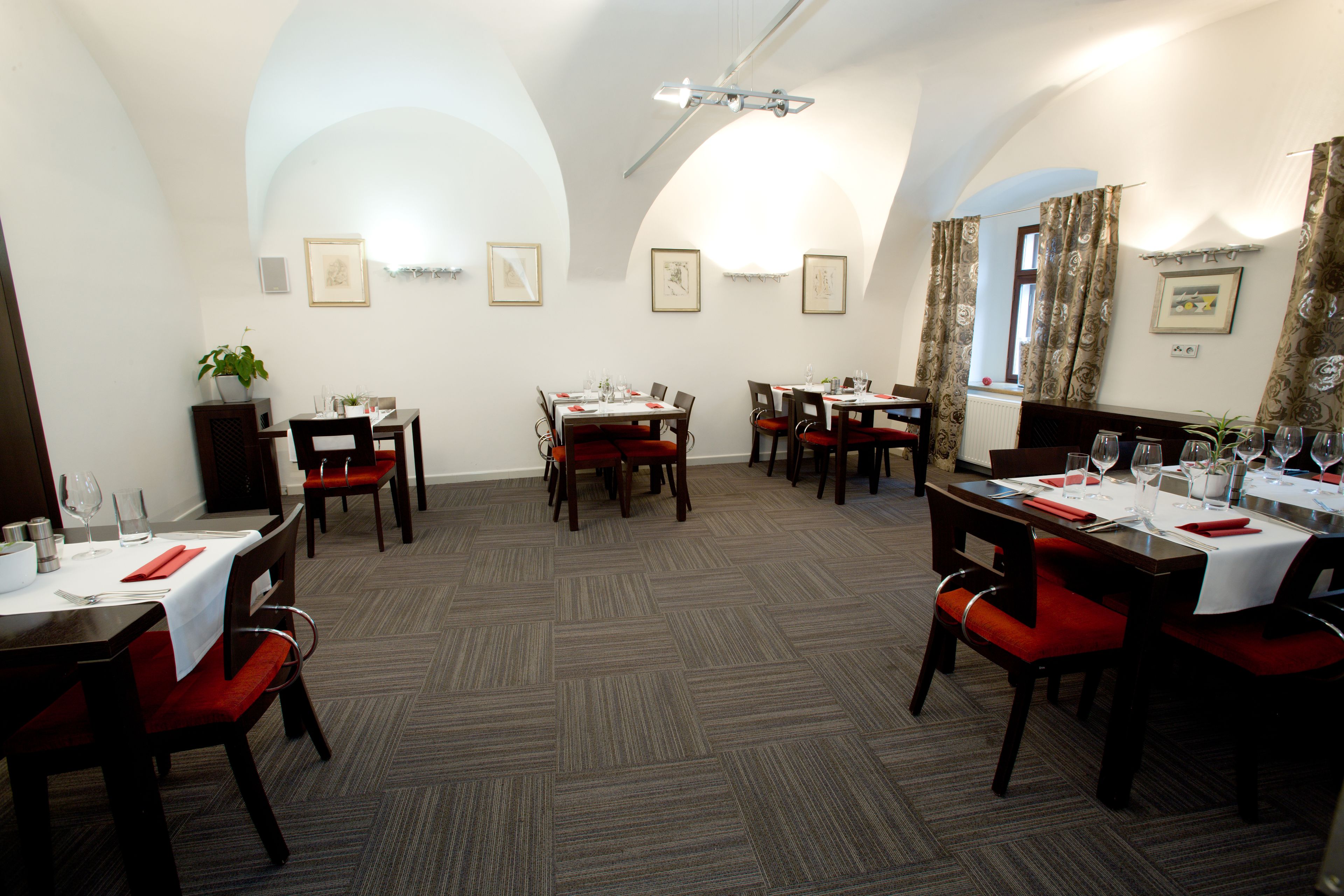 A dining area with multiple tables and chairs, arranged in a spacious layout with a carpeted floor and white walls.