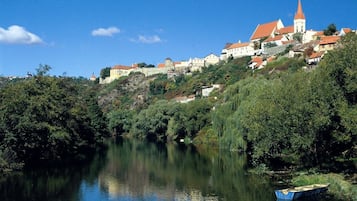 A river with a boat, surrounded by lush greenery and buildings with red roofs.