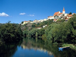 A river with a boat, surrounded by lush greenery and buildings with red roofs. - Hotel Lahofer (Znojmo)