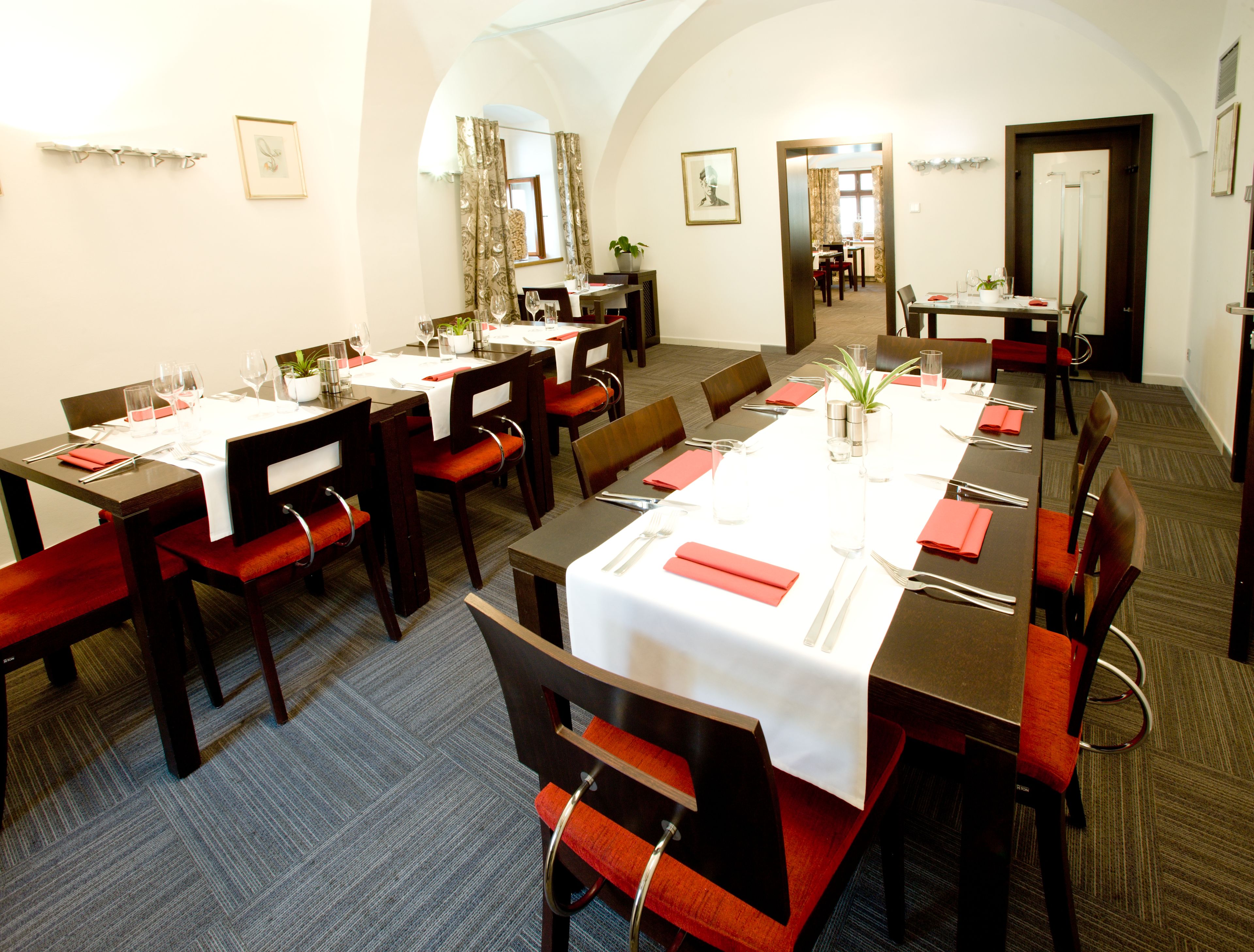 Ein Konferenzraum mit mehreren Tischen, gedeckt für eine Mahlzeit, ausgestattet mit Stühlen, Tischgeschirr und verschiedenen Besteck.
