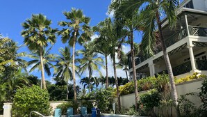 A pool area with palm trees, lounge chairs, and a building with balconies.