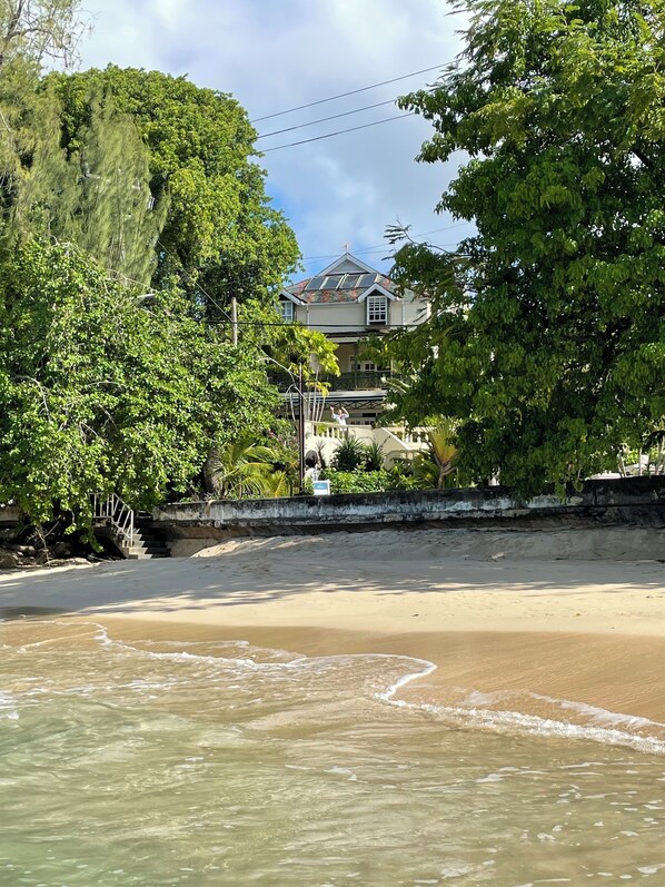 A beachfront property with a sandy beach, a stone wall, and lush greenery.
