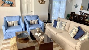 A living room with two blue armchairs, a beige sofa, and a glass coffee table.