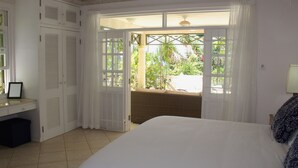 A bedroom with a bed, a desk, a chair, and a window with a view of greenery.
