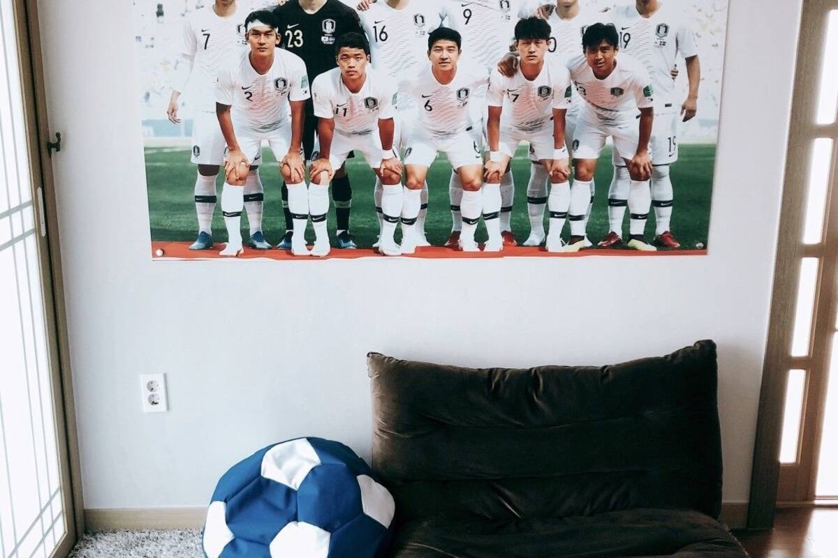 A room with a large poster of a soccer team, a blue and white soccer ball, and a dark brown sofa.
